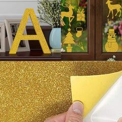 A collage of four images: a gold glittery letter "A" on a table, festive window stickers with deer, a Christmas tree, mittens, a snowman, multipurpose crafts using high-quality A4 Gold and Silver Self-Adhesive Glitter Cardstock Paper for Laser Engraving - 40 Sheets from CrealityFalcon, and a hand peeling back yellow adhesive paper from glittery gold material.