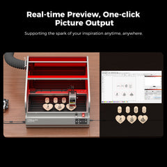 A CrealityFalcon Falcon2 Pro 22W Enclosed Laser Engraver and Cutter Master Engraving Bundle is pictured on a wooden table, with several engraved wooden hearts displayed in front of it. An online interface for designing engravings is shown on a computer screen beside the machine, showcasing its cutting-edge Pilot Technology. Text above reads: "Real-time Preview, One-click Picture Output.